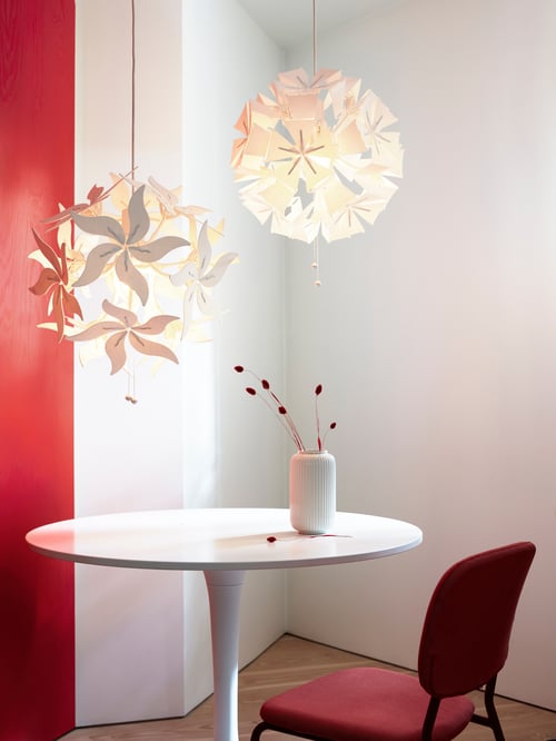 A room with two RAMSELE pendant lamps in white, hanging above a round white table with a vase and reeds, and a red chair.