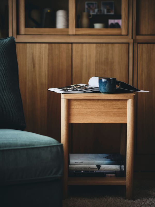 An oak veneer TONSTAD bedside table stands beside a chair in front of an oak veneer TONSTAD storage combination.