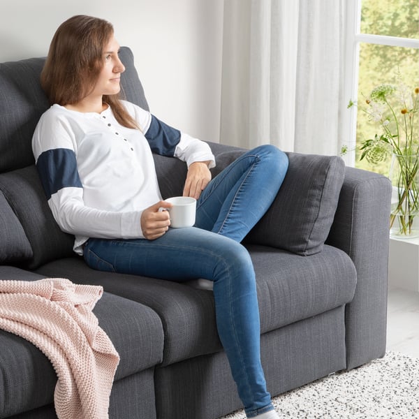 Kobieta siedząca na ciemnoszarej sofie ESKILSTUNA i pijąca kawę.