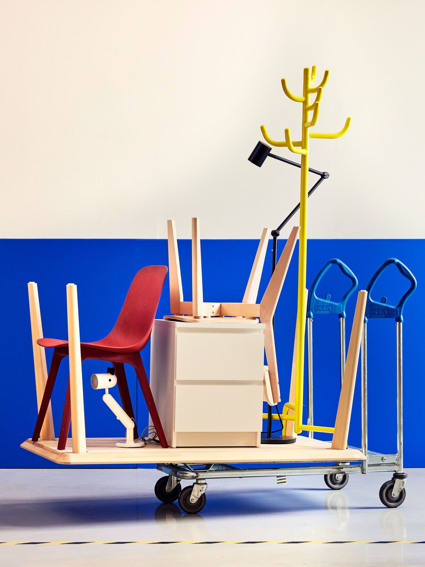 Mobilier et équipement de bureau empilés sur un chariot à roulettes, comprenant une chaise, un caisson à tiroirs, un porte-manteau et un diable, sur fond bleu et blanc.