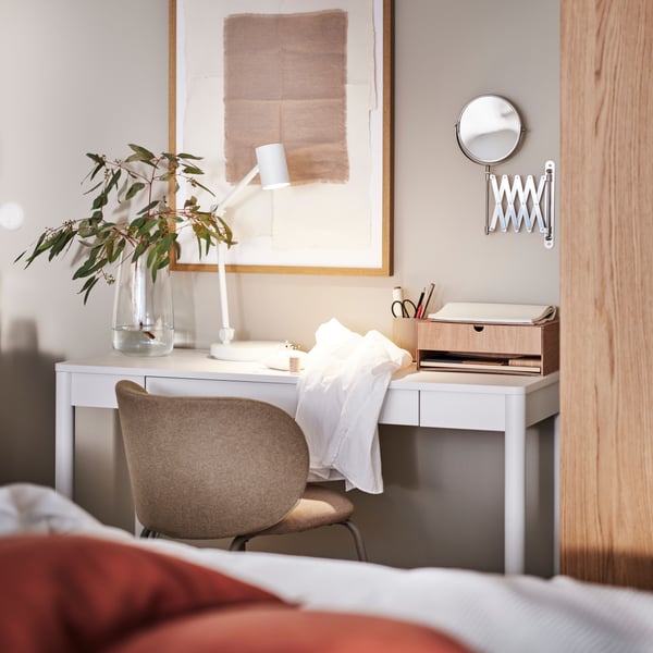 An off-white TONSTAD desk with various items on top by a PAX/TONSTAD wardrobe and with a dark beige KRYLBO chair in front.