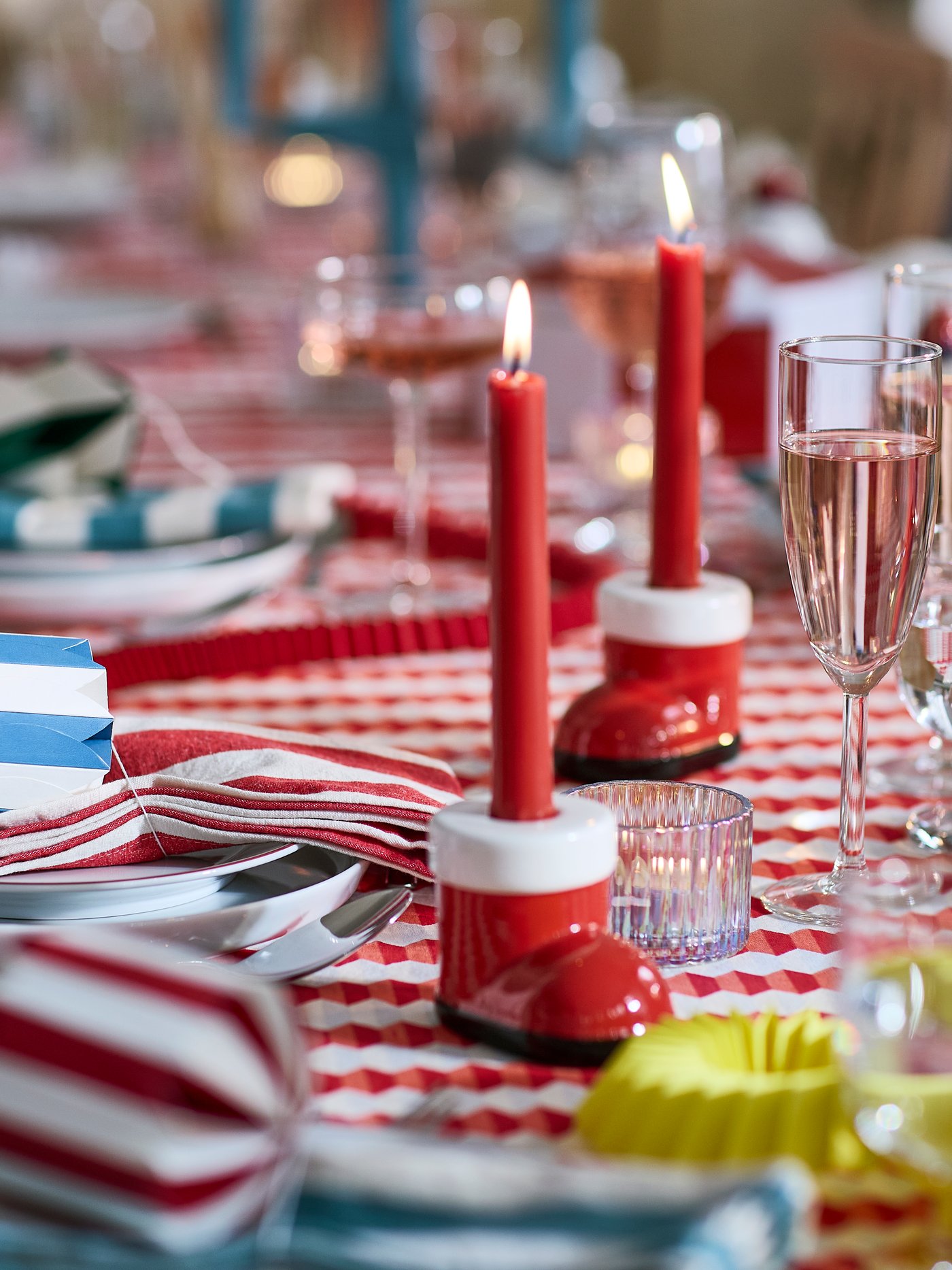 Weihnachtlich gedeckter Tisch mit roten Kerzen in Kerzenhaltern, gestreifter Tischdecke und Glasgeschirr.