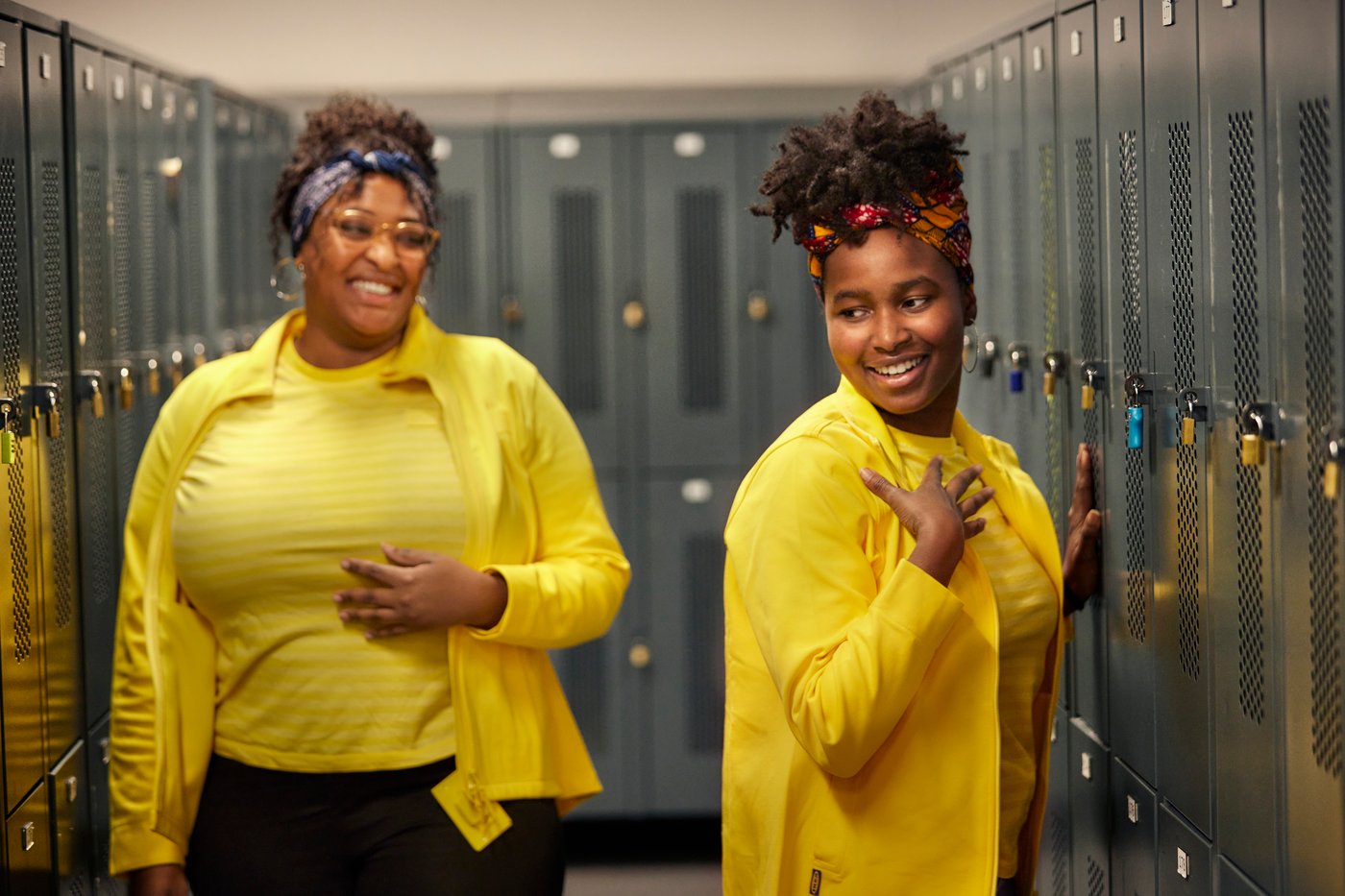 Dwie czarne, uśmiechnięte kobiety w żółtych strojakch praconiczych IKEA w szatni pracowniczej. 