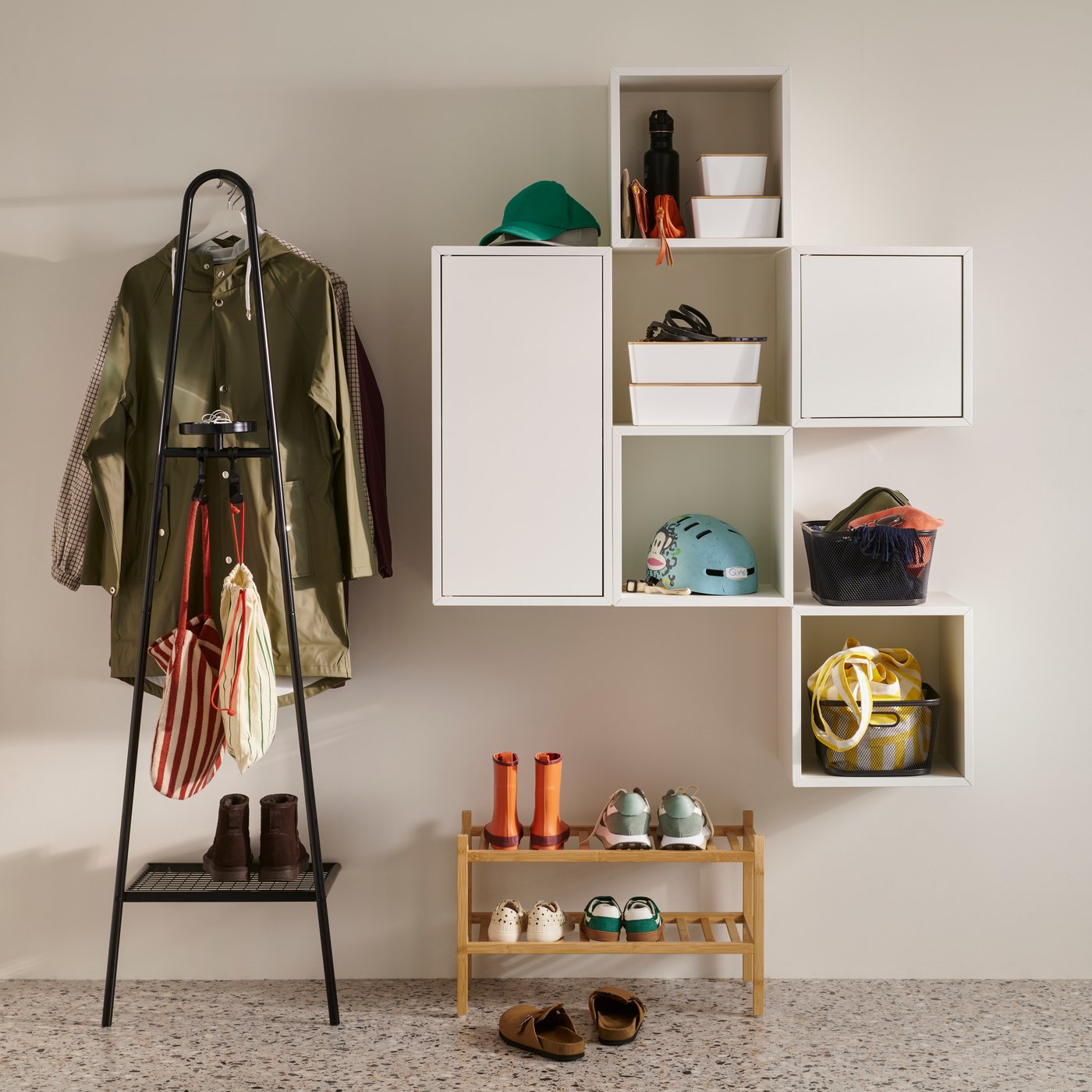 A neat hallway with coats on a black ÄLGANÄS clothes rack and open and closed white EKET wall cabinet units.