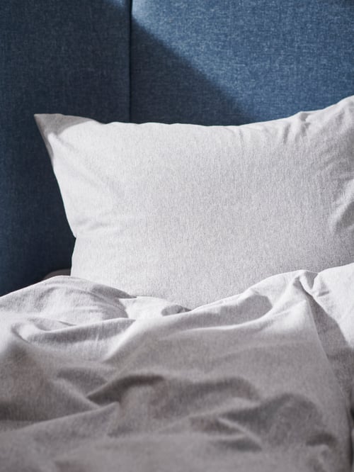 Un lit doté d’une tête haute bleue est garni de linges de lit SPJUTVIAL gris clair et multicolores.