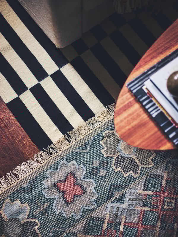 A STOCKHOLM coffee table with walnut veneer placed on a VESTERVIG flatwoven rug and a striped STOCKHOLM flatwoven rug.