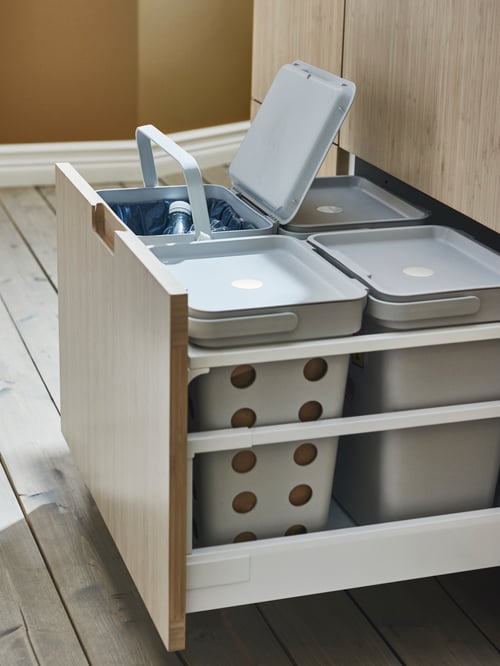 Prim-plan de bucătărie al unei soluții de sortare a deșeurilor de culoare gri deschis dreptunghiular din plastic polipropilenă, în spatele unui sertar frontal.