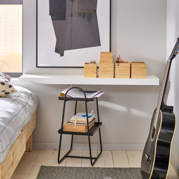 Bedroom with wall mounted LACK bench with wooden boxes. HATTÅSEN bedside table/shelf unit, guitar leaning against wall.