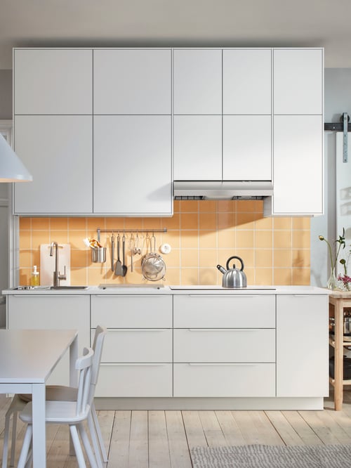 Une cuisine moderne comprenant une élégante armoire inférieure en bois blanc à trois façades et à trois tiroirs, quelques armoires murales et un dosseret jaune.