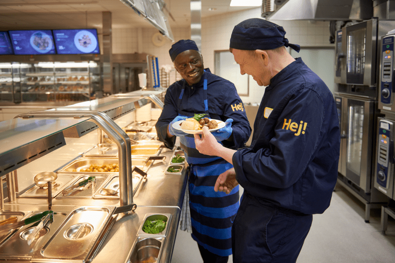 Kaksi IKEA-työntekijää ravintolan linjaston takana työskentelemässä.