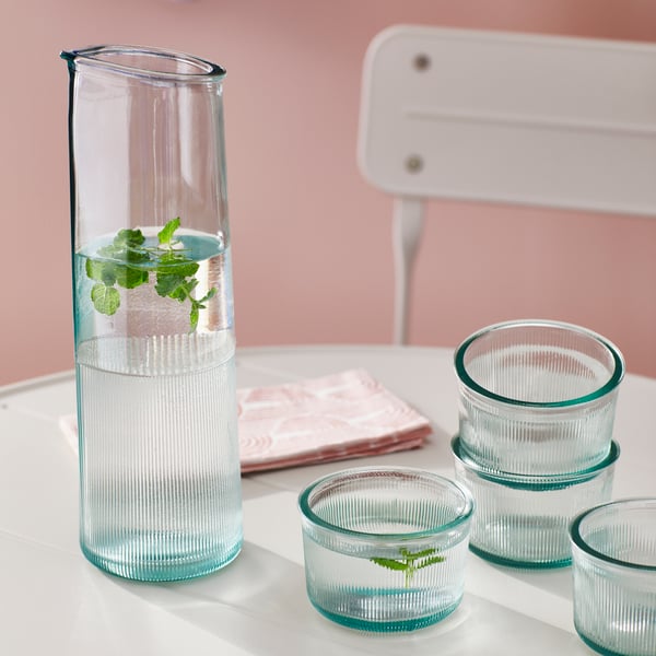 A BERGVATTNET carafe, glasses, and a napkin are placed on an off-white SUNDSÖ table with a folding chair next to it.