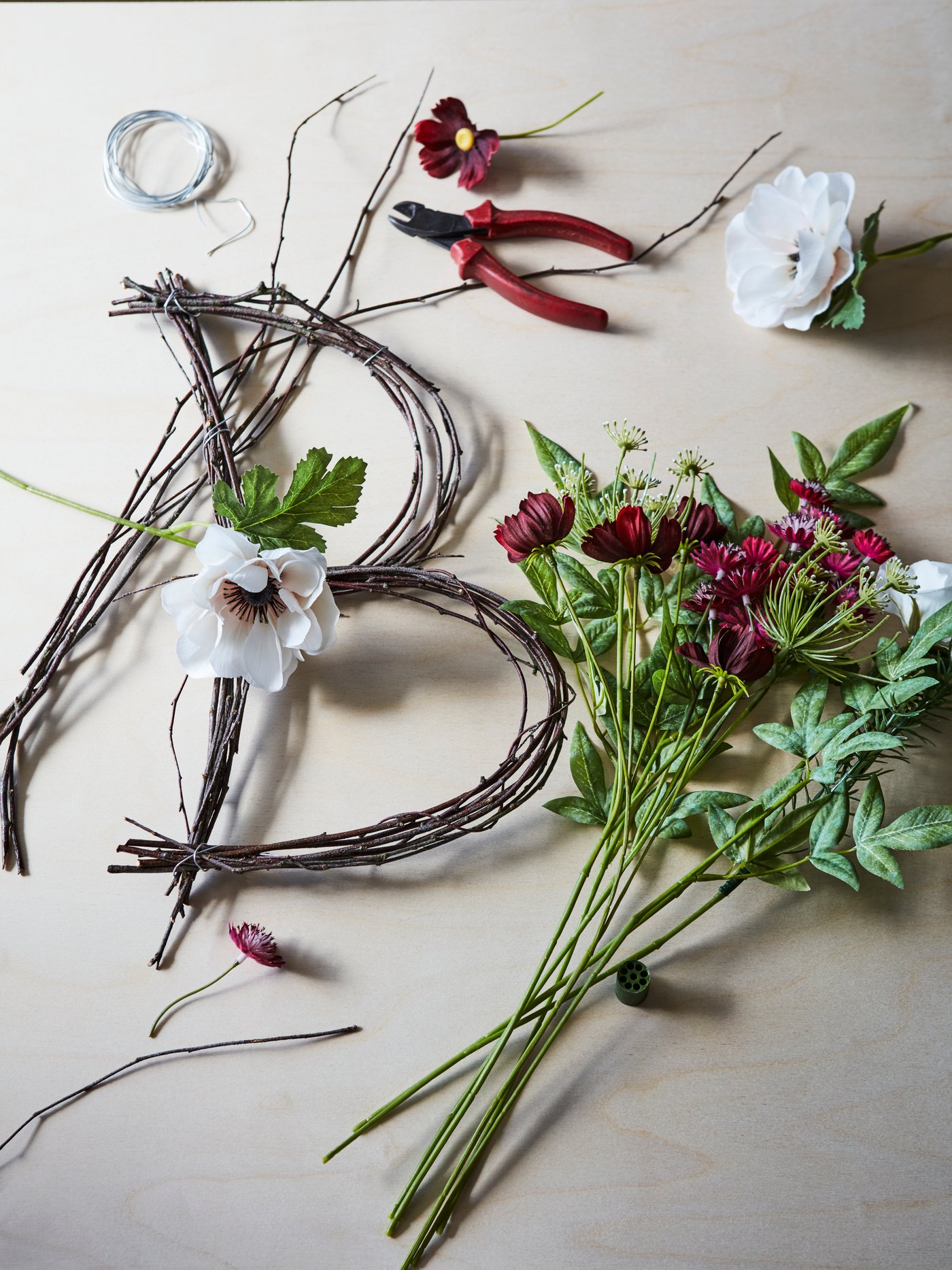 Fleurs et brindilles utilisées pour former une décoration florale en forme de lettre B, posées sur une surface à côté d’une pince.