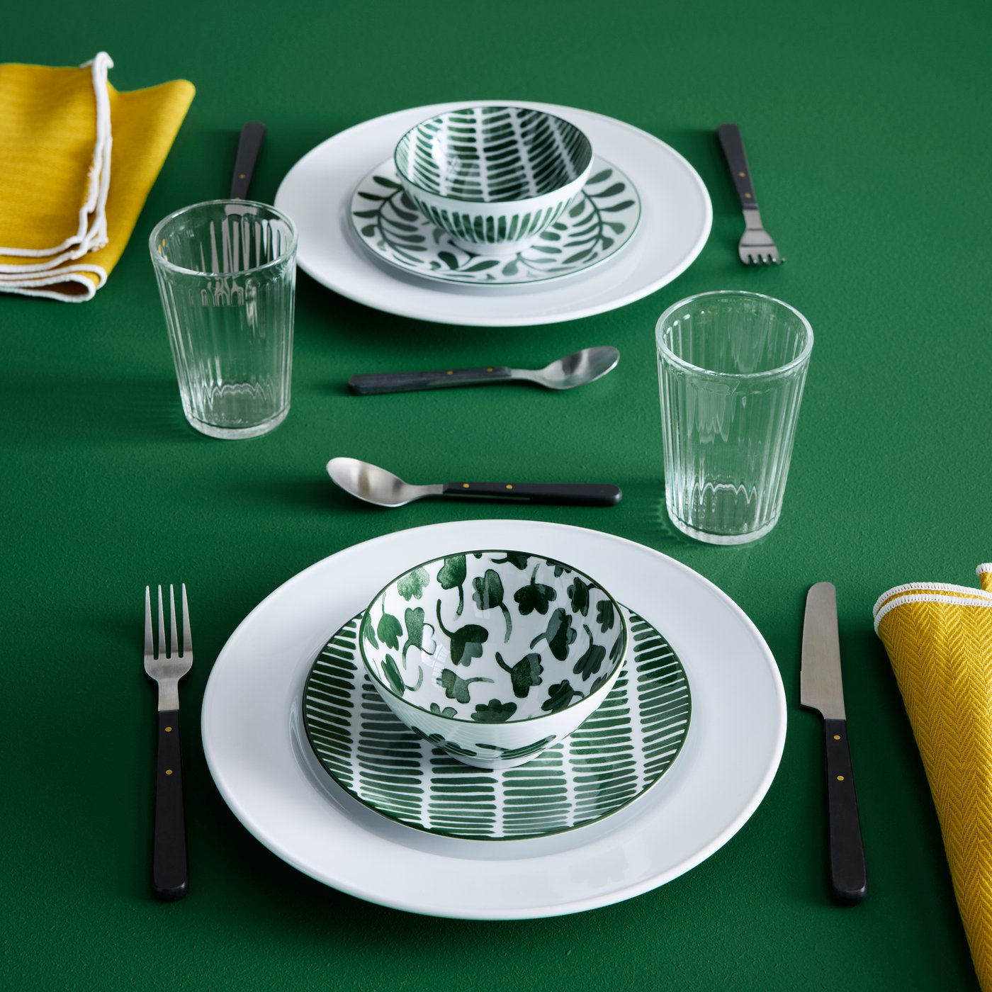 A table setting features white VARDAGEN plates, patterned ENTUSIASM bowls, glasses and cutlery all placed on a green surface.