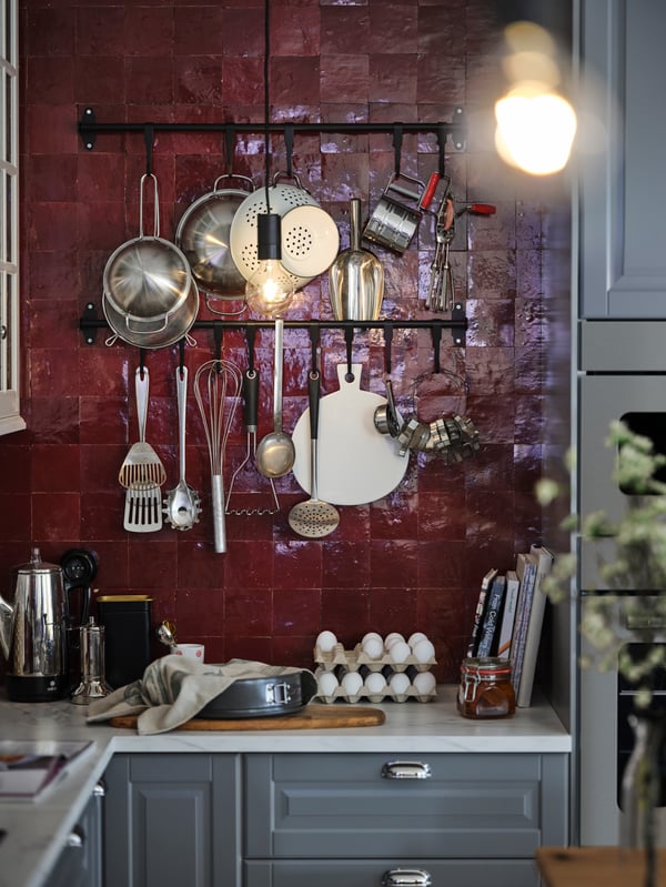 Multiple utensils hanging from black HULTARP rails in a red-tiled kitchen with a white marble-effect worktop and grey fronts.