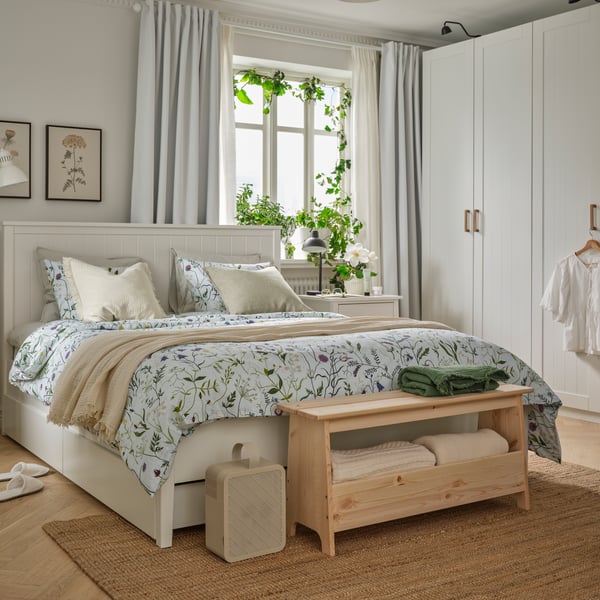 A bedroom featuring a white GULLABERG bed frame with four storage boxes and MATTOXBÄR bedding beside a window with plants.