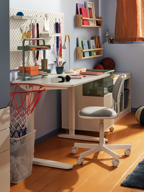 A white RELATERA sit/stand desk combination in a light blue room with a white SKÅDIS pegboard on the wall above it.