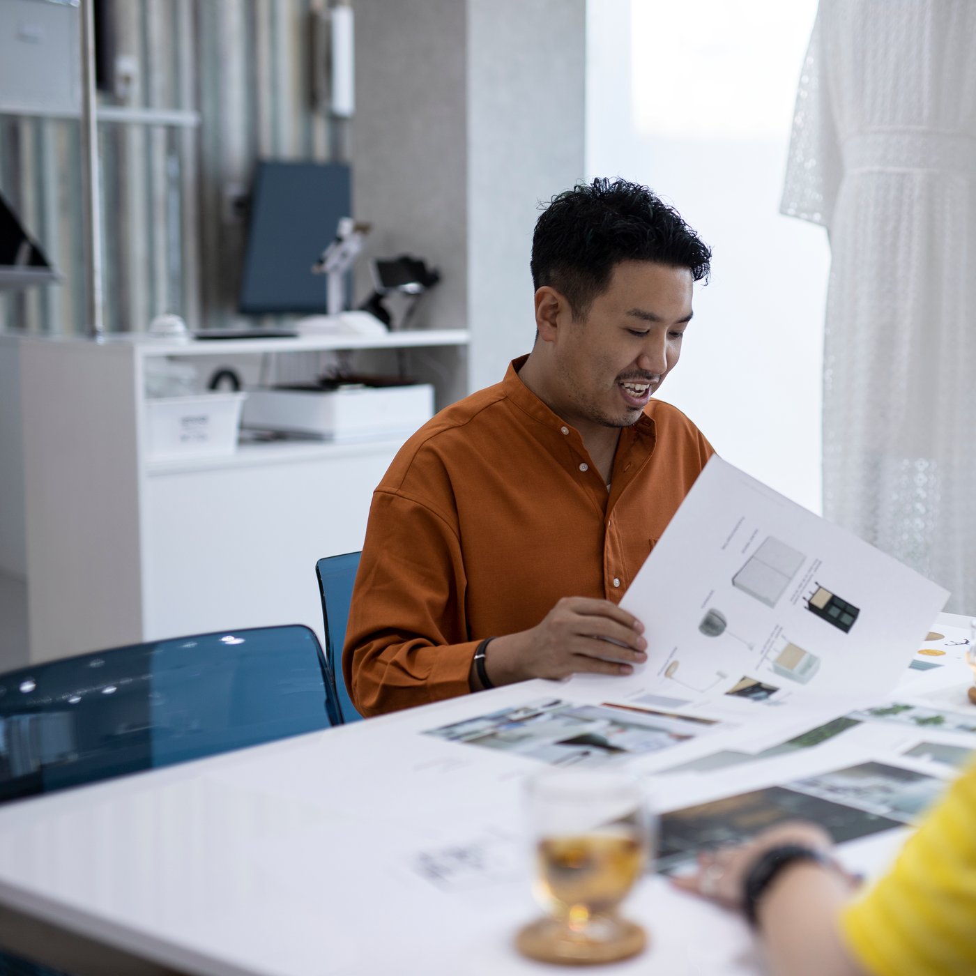 A man holding up a catalog of IKEA furniture is smiling at a table with others.