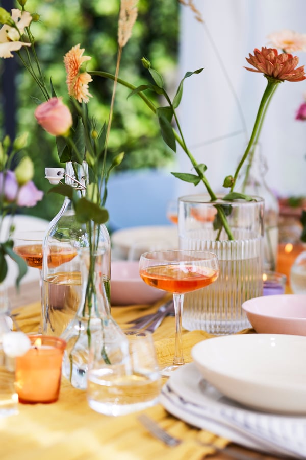 Una tavola imbandita con piatti, vari bicchieri e diversi vasi di fiori con fiori singoli e non erbe.