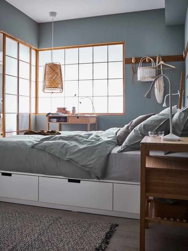 NORDLI bedframe with storage in a bedroom with green BERGPALM duvet covers and sheets on a bed. A VINDUM rug is laid over the floor beneath the bed frame, with a NORDKISA bedside table standing next to the bed.  