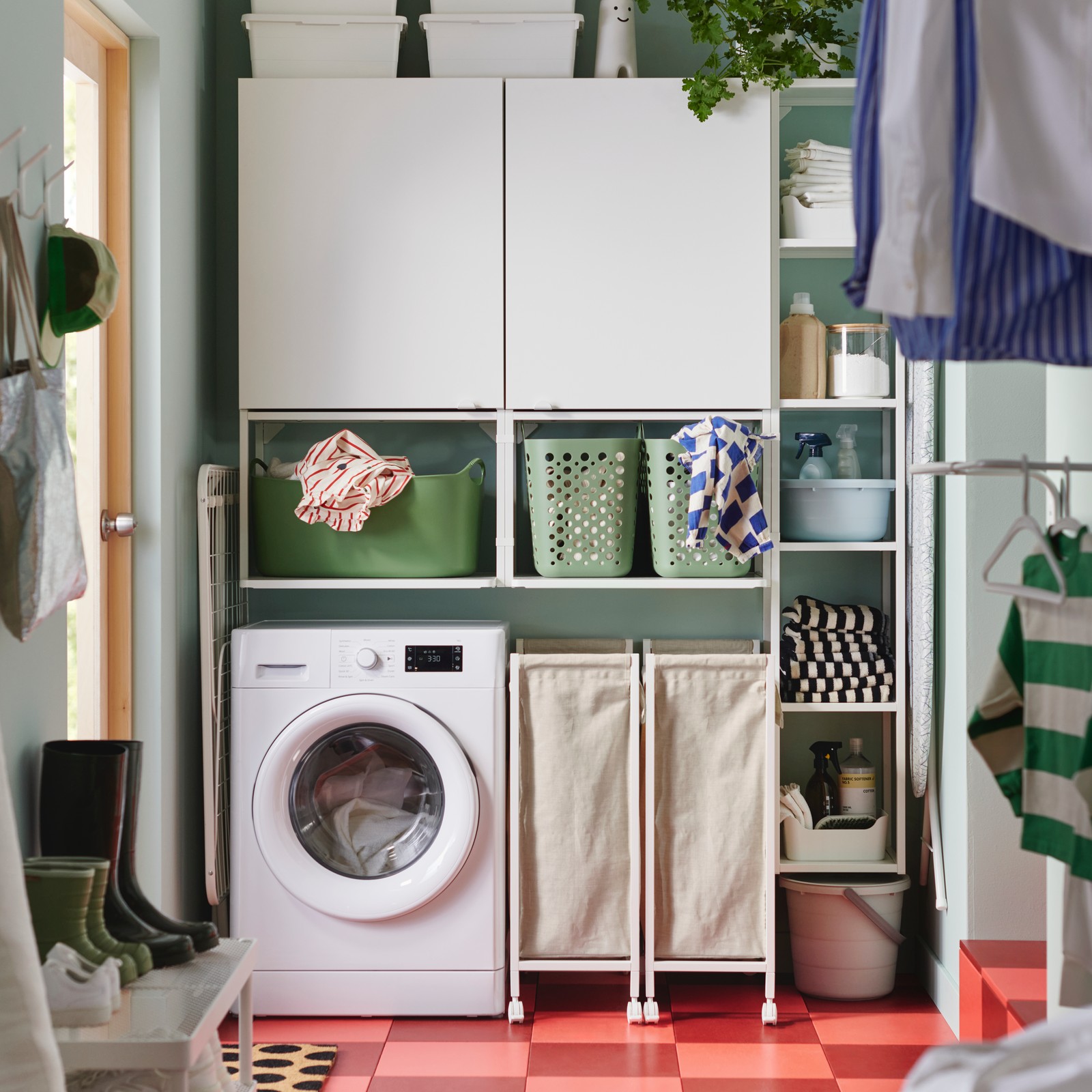 En hvit ENHET oppbevaringskombinasjon med vegghyller og skap over en vaskemaskin i et lyst, moderne klesvaskområde.