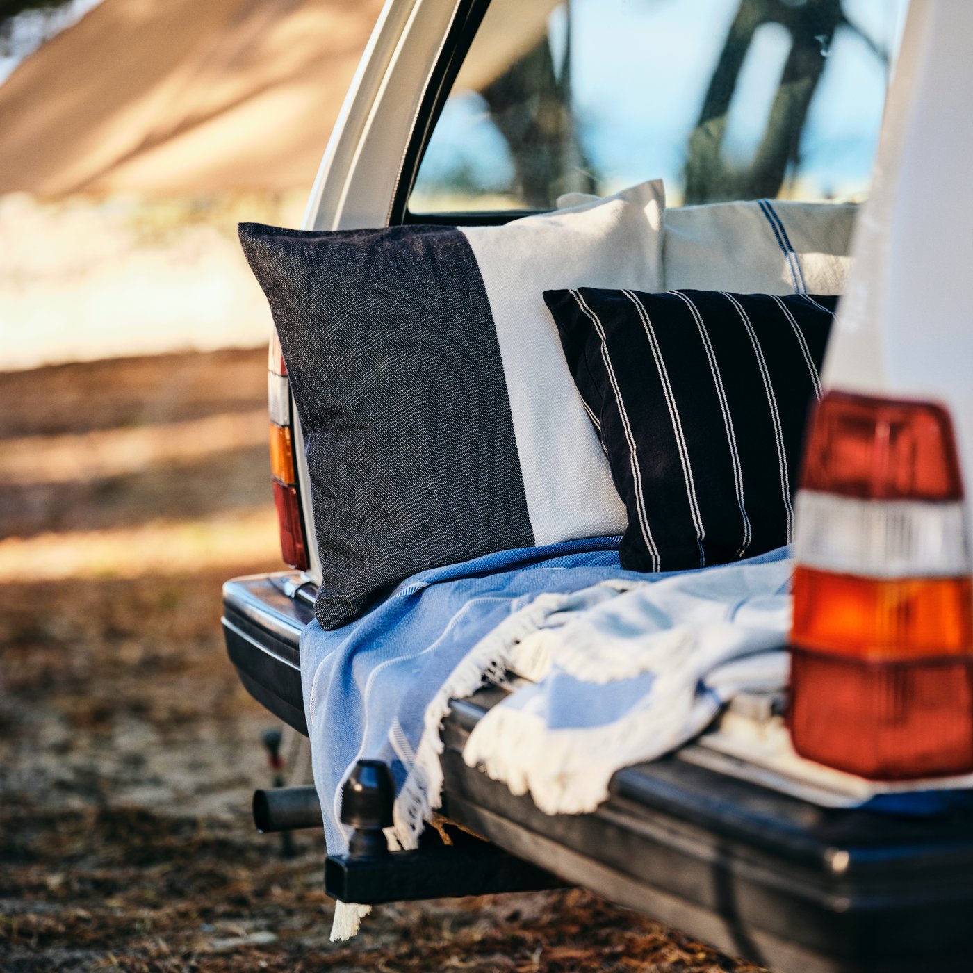 Car trunk opened to reveal a cosy setup with the SOLUPPGÅNG throw and cushion covers, perfect for comfortable outdoor relaxation.