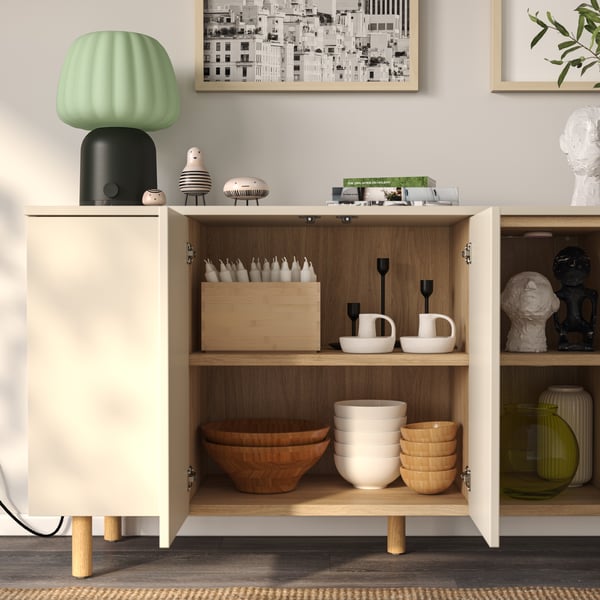 A light grey-beige LEDAMOT cabinet has its doors open, showing a storage section filled with stacked bowls and candles.