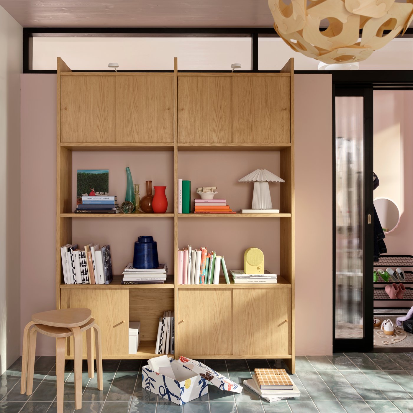A bright living room with a light oak-effect LÅDMAKARE storage combination with sliding doors with books and decoration.