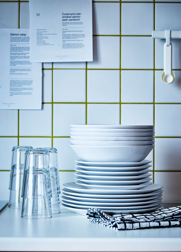 A VÄRDERA dinnerware set sitting on top of a white countertop next to VARDAGEN glasses. There are white tiles in the background.