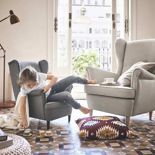 A girl is sitting on a mini armchair and playing with a tea set.
