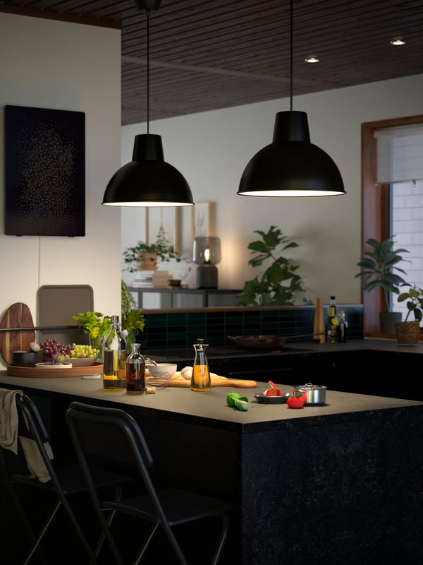 Two black SKURUP hanging pendant lamps are lighting up a kitchen island with a KASKER countertop in anthracite stone effect.