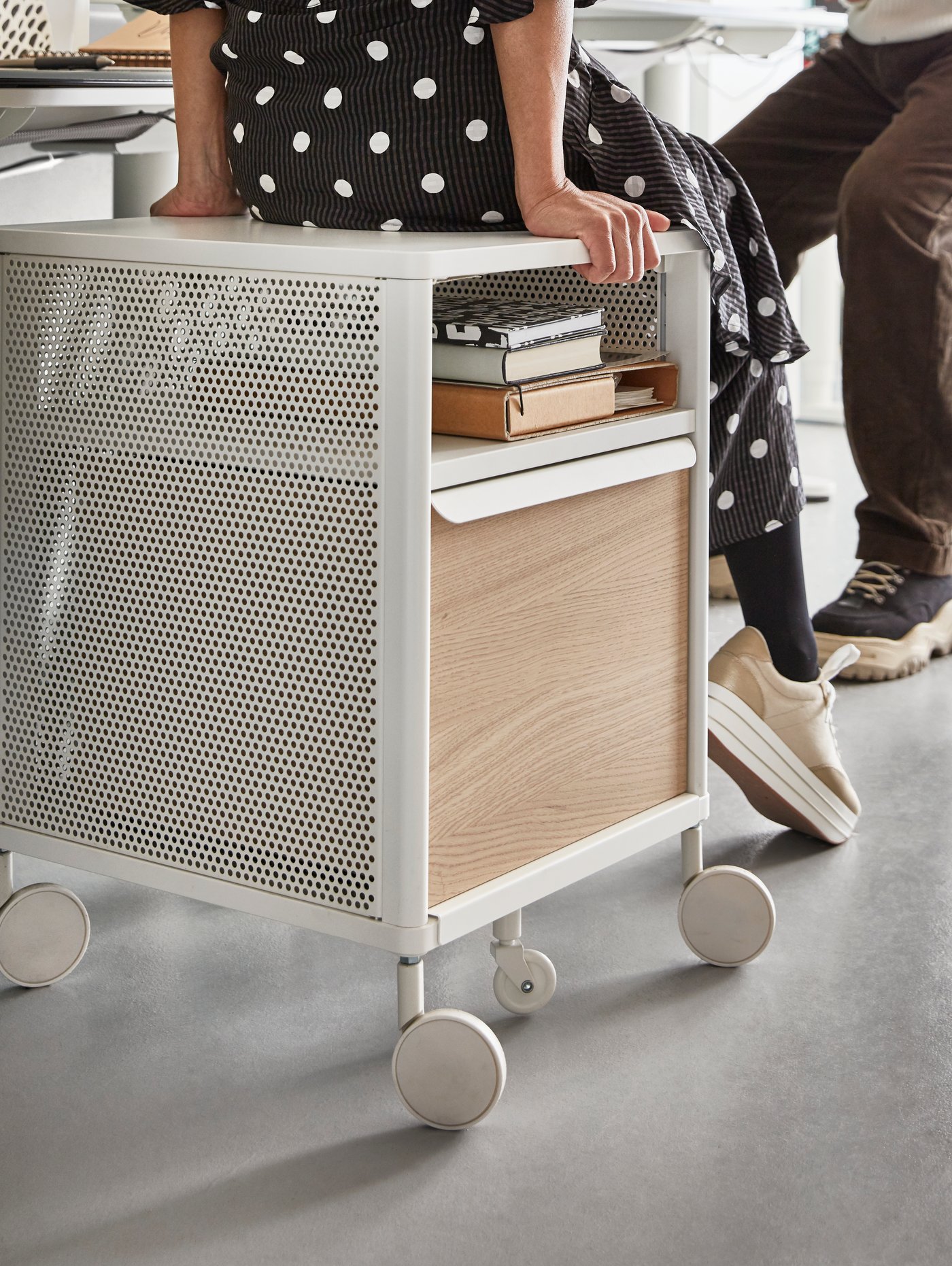 Mujer sentada sobre una mesa-carrito móvil BEKANT con almacenamiento en su interior.