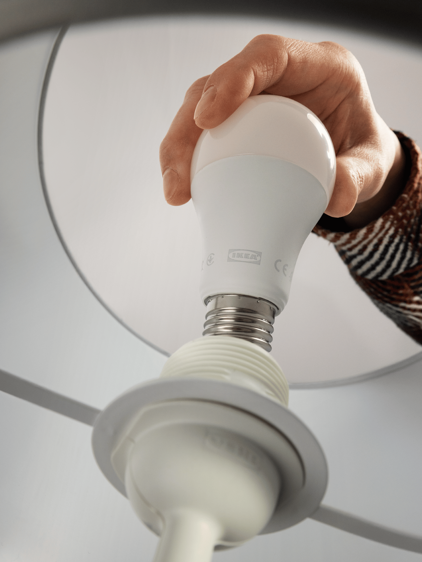 Henkilö asettaa valkoista E27 LED-lamppua valaisimeen.