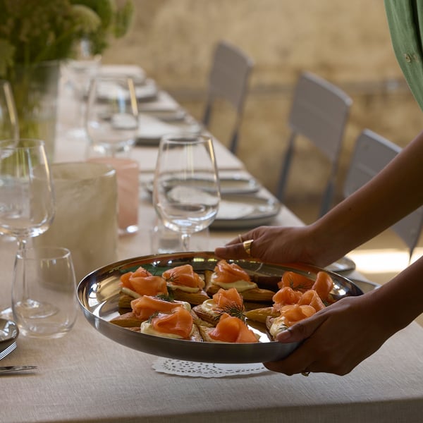 Personne qui apporte un plateau de toast au saumon sur une table posé avec des verres STORSINT