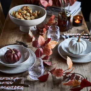 A dining table adorned with a HÖSTAGILLE artificial garland in mixed colours, surrounded by elegant dishes and glassware.