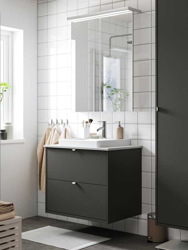 A dark gray HAVBÄCK vanity cabinet with two drawers has a tall HAVBÄCK cabinet next to it and a mirror cabinet with above it.
