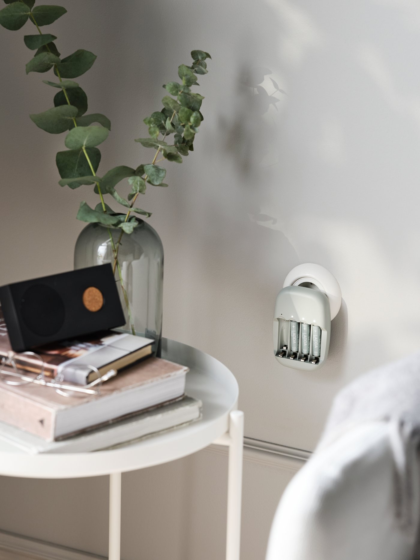 A STENKOL battery charger with three LADDA rechargeable batteries in it sits in a wall socket near a GLADOM tray table.