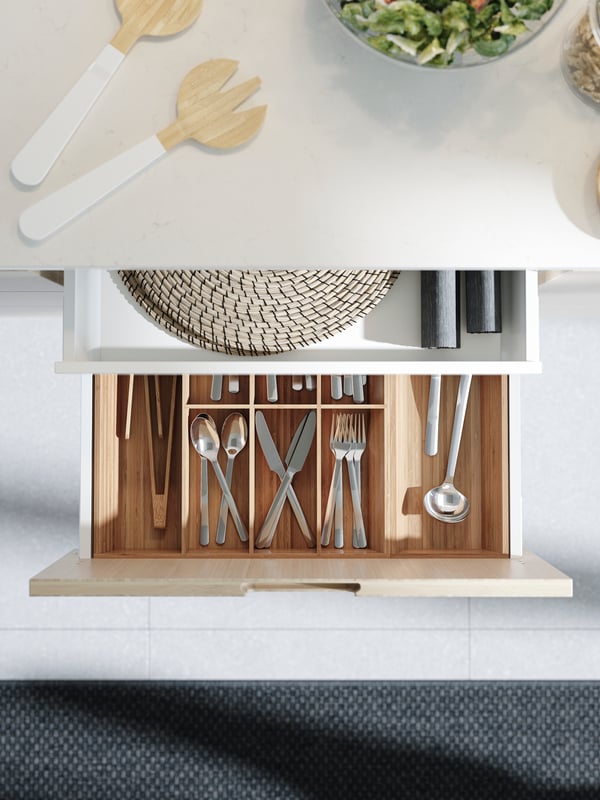 An open kitchen drawer with a cutlery tray in bamboo. Cutlery and different kitchen utensils are stored and divided here.