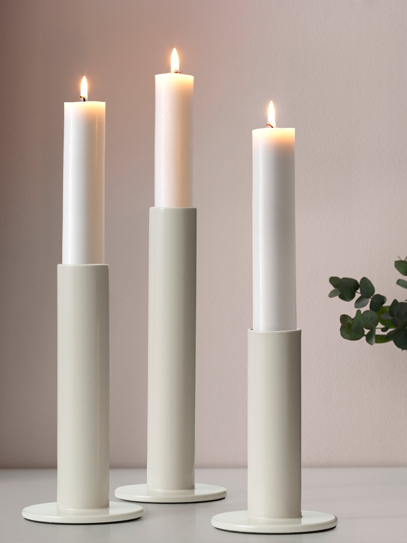 Drei TUVKORNELL Kerzenständer in off-white mit weißen Stabkerzen.
