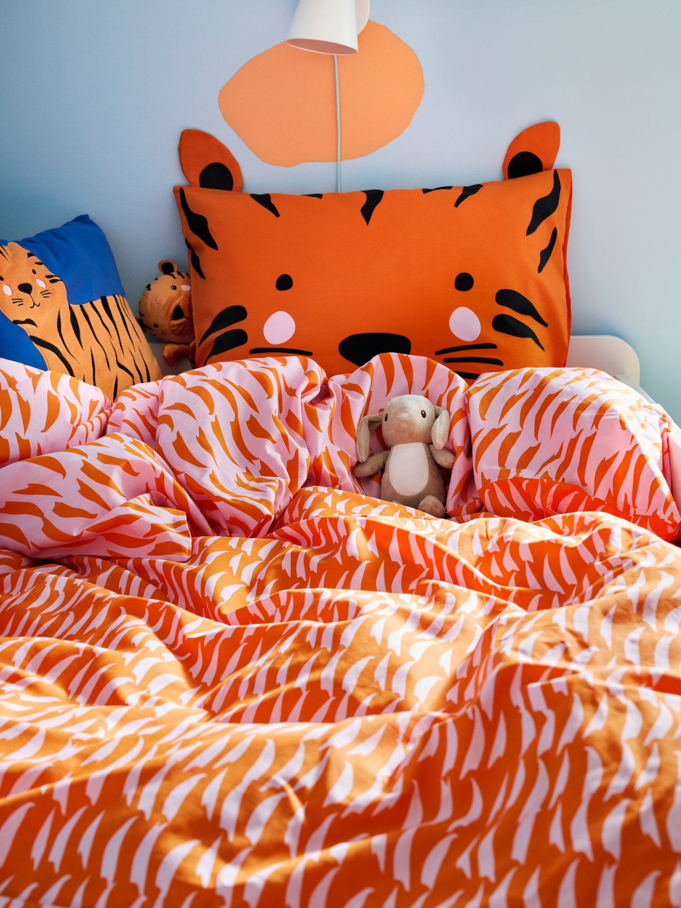 Nahaufnahme von NATTHÄGER Bettbezug und Kissenbezug mit orangefarbenem Tiger, ein kleines DVÄRGHARE Plüschkaninchen chillt im Bett.