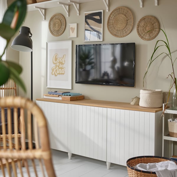 A poster in a KNOPPÄNG frame and three GILLSTAD wall decorations hang on a wall near a TV above a BESTÅ storage combination.