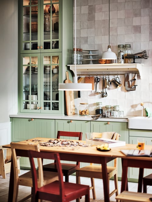 Eclectic kitchen with wooden table and chairs, and kitchen cabinets with light green drawer fronts with a lacquered finish.