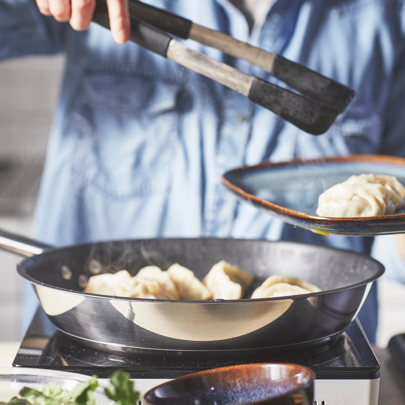 En person kledd i skjorte, steker dumplings i en stekepanne i rustfritt stål.