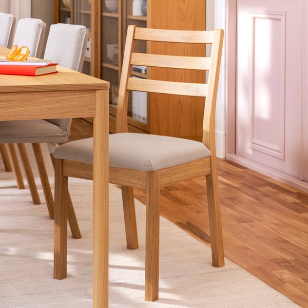 The corner of a TONSTAD table in oak veneer, with various TONSTAD chairs beside it, the table has a red book place on it.