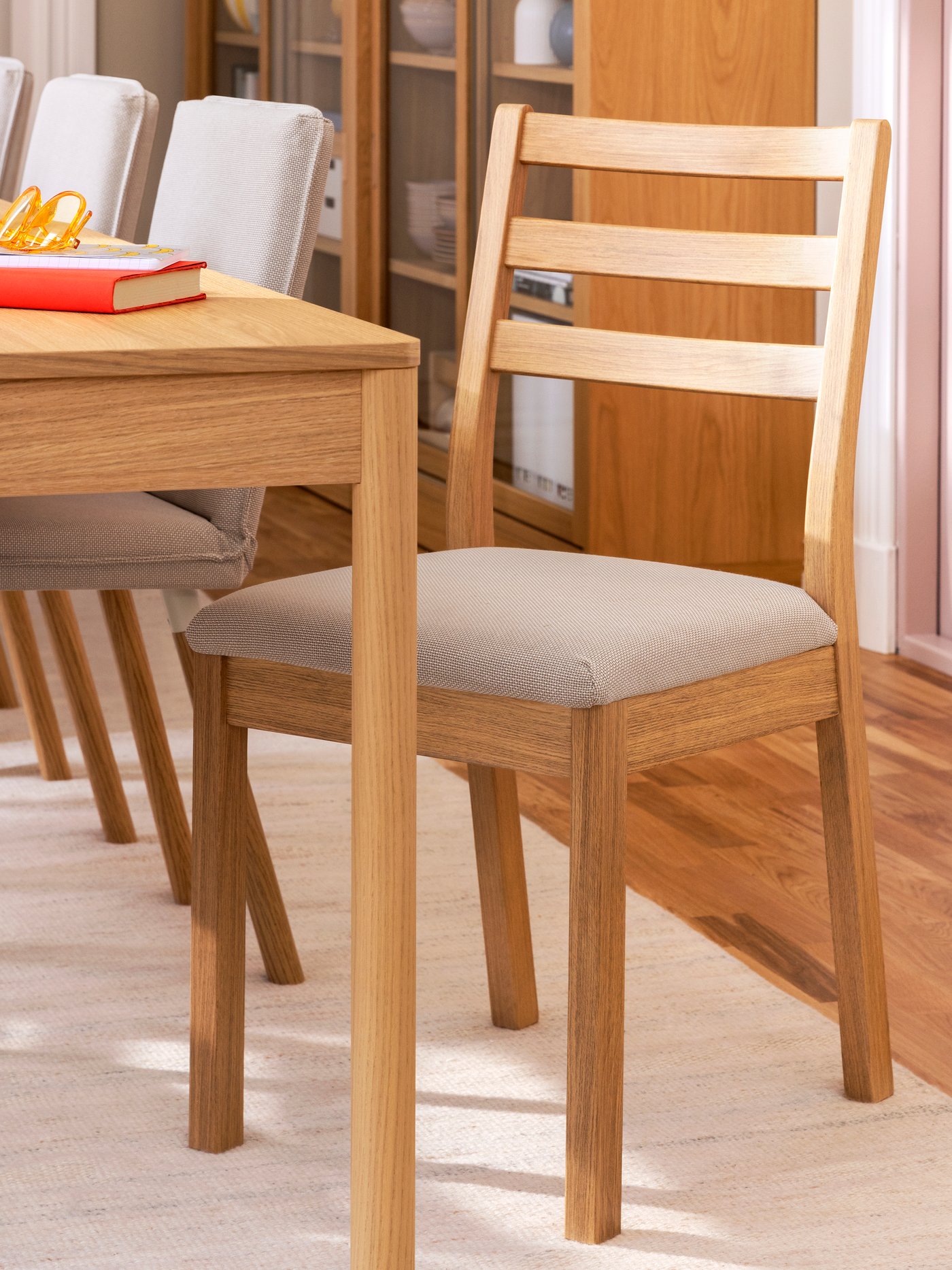 The corner of a TONSTAD table in oak veneer, with various TONSTAD chairs beside it, the table has a red book place on it.