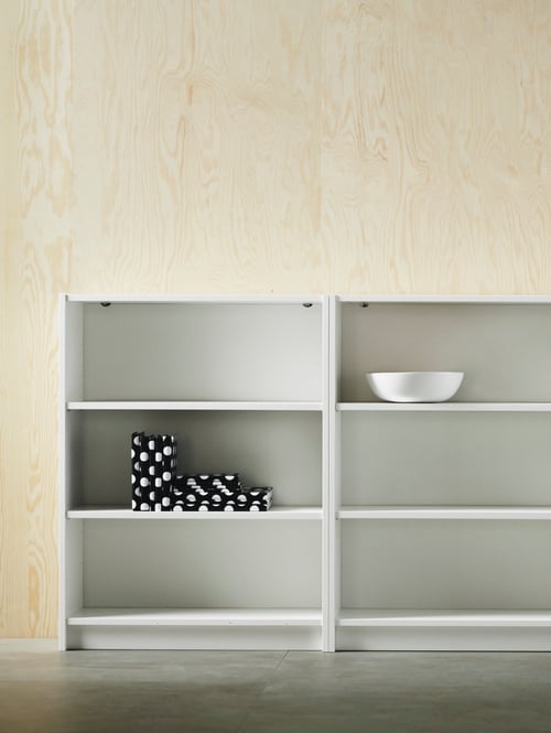 Room with light wood wall panels, dark grey floor and white wooden bookcase with white bowl and black and white napkins.