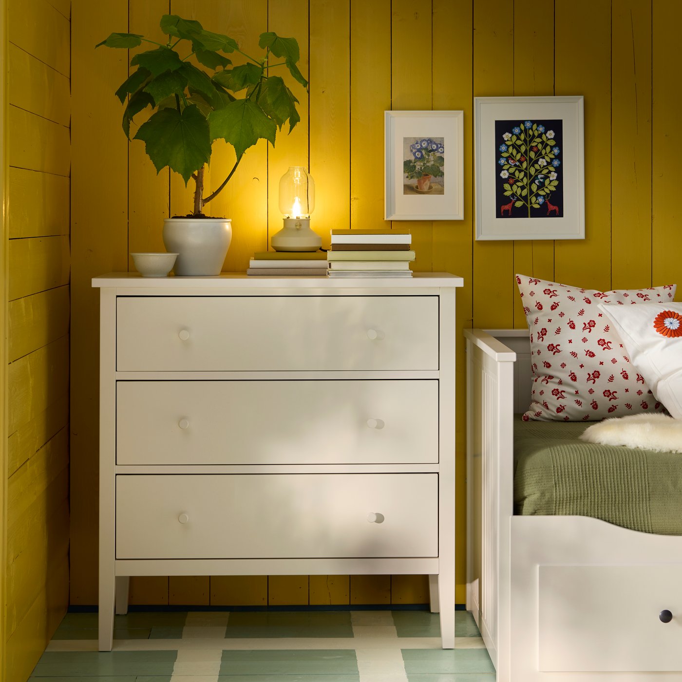 En vit GULLABERG byrå med tre lådor i ett rum med gula väggar, med en TÄRNABY bordslampa och en krukväxt ovanpå.
