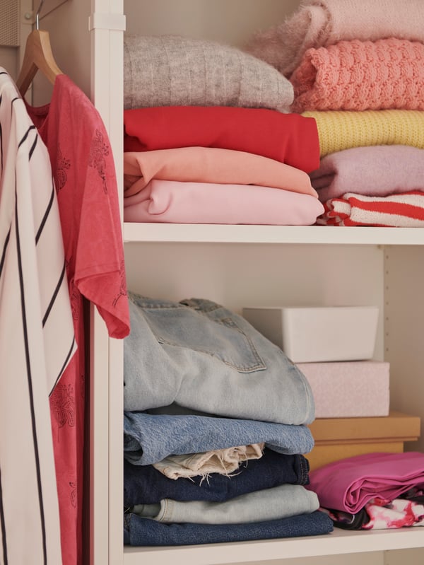 A close-up of the hanging rail and shelves of a PLATSA wardrobe with clothes on BUMERANG hangers and folded on the shelves.
