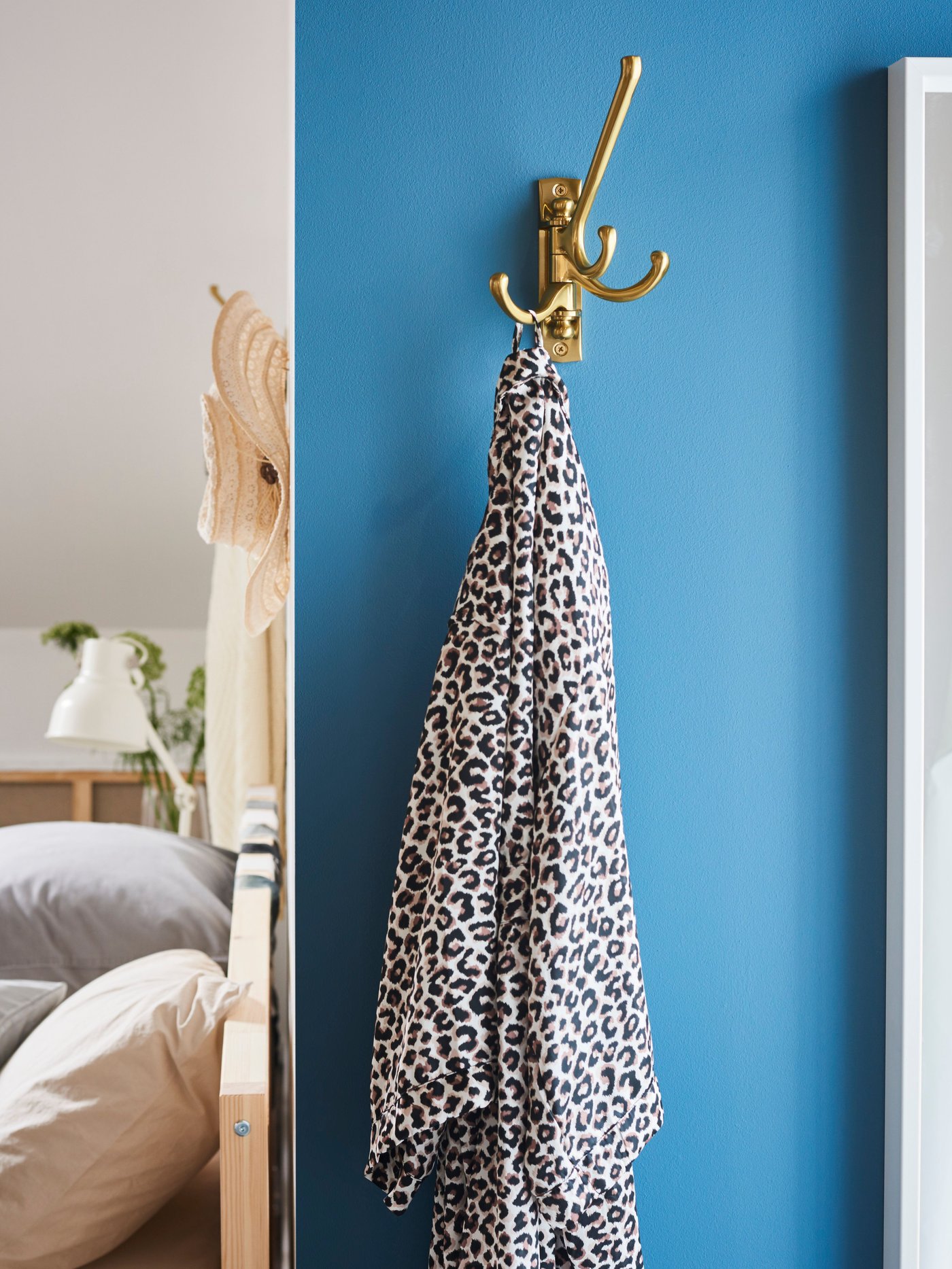 An animal print scarf hangs on a brass-coloured KÄMPIG 3-armed swivel hook that is on a light blue wall by a bed.