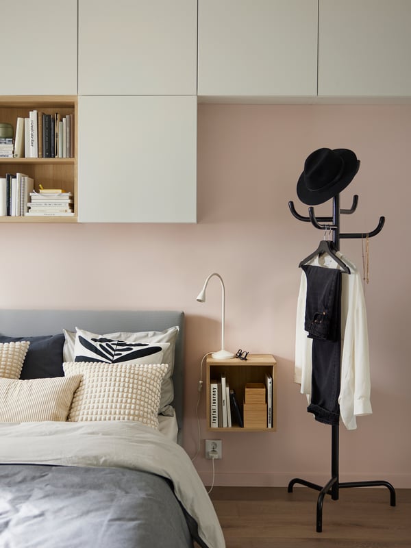 Un appendiabiti BONDSKÄRET giallo vicino a un letto GLADSTAD grigio con tessili nei colori grigio e panna, con un mobile EKET vicino.