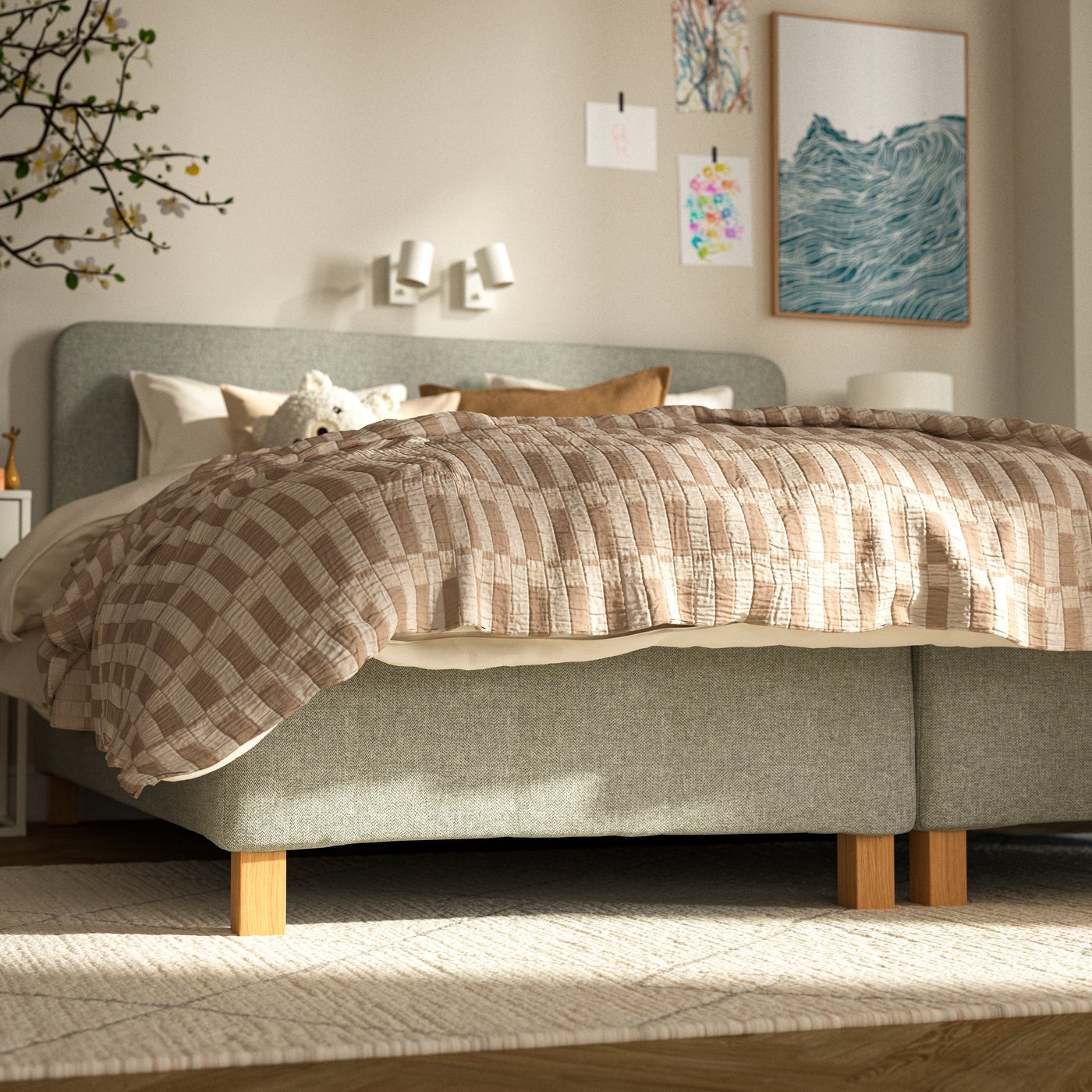 RÅHOLMAR resårbotten med träben och matchande huvudgavel, bäddad med rutigt överkast i beige toner. Sängen står i ett ljust sovrum med tavlor på väggen och en matta på golvet.
